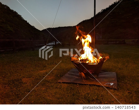 Enjoying a bonfire and outdoor scenery at a nature-rich campsite at dusk. Enjoying a bonfire and outdoor scenery at a nature-rich campsite at dusk. 140718543