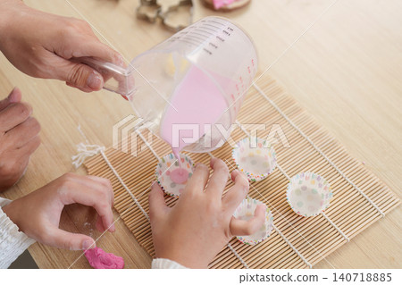 Cropped hands pouring pink batter into cupcake liners for home baking Cropped hands pouring pink batter into cupcake liners for home baking 140718885