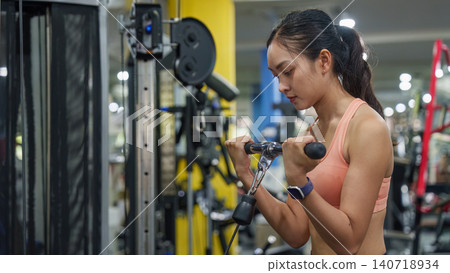Asian woman doing bicep curls on cable machine for arm strength training 140718934