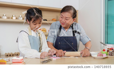 Asian grandmother smiling at granddaughter using cookie cutter in kitchen Asian grandmother smiling at granddaughter using cookie cutter in kitchen 140718935