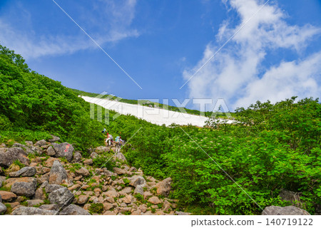 晴朗的夏日,登山者的背影沿著白馬乘鞍山陡峭的岩石山坡行進,遠眺白雪皚皚的山景。 晴朗的夏日,登山者的背影沿著白馬乘鞍山陡峭的岩石山坡行進,遠眺白雪皚皚的山景。 140719122