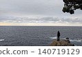 The setting sun sinking into the sea and the silhouette of a person standing there. 140719129