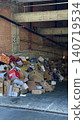 Pile of cardboard boxes and paper waste photo in unfinished building garage, messy recycling storage with construction walls, urban trash, packaging, disposal and environmental cleanup concept 140719534