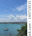 Sailboat on turquoise sea photo with coastal town, dramatic white clouds and blue sky, peaceful summer travel landscape for seaside vacation, tourism, sailing, nature and marine design 140719535