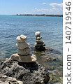 Balanced stone stacks on rocky seashore photo with turquoise sea, distant coastal town and blue sky, peaceful summer travel landscape for meditation, nature, balance, vacation and wellness design 140719546