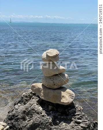 Balanced stones on rocky seashore photo with calm blue sea, clear sky and distant sailboat, peaceful coastal landscape for travel, summer vacation, meditation, balance, nature and wellness design Balanced stones on rocky seashore photo with calm blue sea, clear sky and distant sailboat, peaceful coastal landscape for travel, summer vacation, meditation, balance, nature and wellness design 140719551