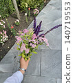 Hand holding fresh wildflower bouquet photo with pink and purple flowers on city sidewalk near garden bed, natural summer floral arrangement for lifestyle, nature, gardening and outdoor design 140719553