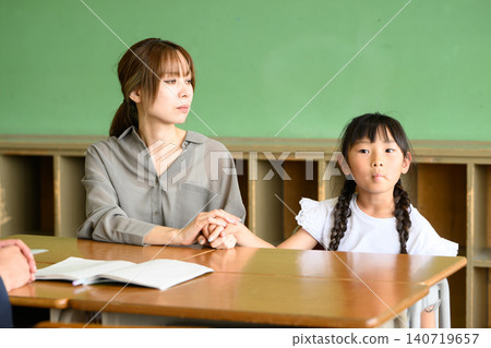 A mother and her daughter are having a friendly and cheerful three-way meeting (consultation) with the teacher in an elementary school classroom. A mother and her daughter are having a friendly and cheerful three-way meeting (consultation) with the teacher in an elementary school classroom. 140719657