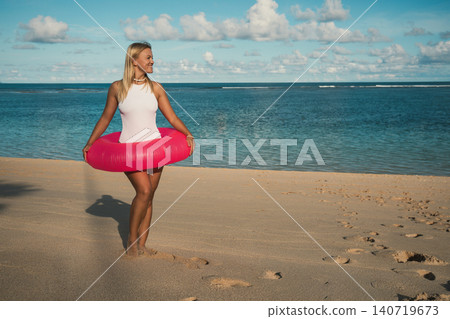 Woman stands on sandy beach with pink float in water Woman stands on sandy beach with pink float in water 140719673