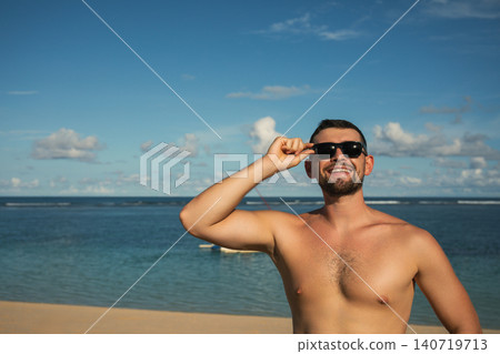 Man smiles while standing on a beach during summer time Man smiles while standing on a beach during summer time 140719713