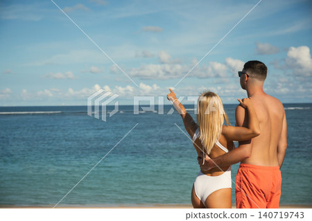 Couple looks out at the ocean and points towards the horizon Couple looks out at the ocean and points towards the horizon 140719743