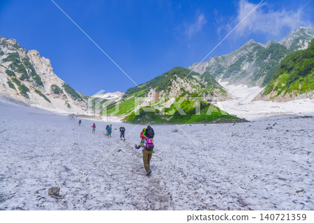 A clear summer day: A line of hikers looking up from the lower part of the Hakuba Daisekkei (Hakuba Great Snow Valley) and the majestic Hakuba-dake mountain rising against the blue sky. 140721359