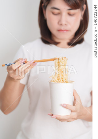 Happy young Asian woman enjoying a delicious cup of hot instant noodles while relaxing at home, Cheerful female eating instant ramen with a smile at apartment. Simple lifestyle and quick meal concept Happy young Asian woman enjoying a delicious cup of hot instant noodles while relaxing at home, Cheerful female eating instant ramen with a smile at apartment. Simple lifestyle and quick meal concept 140722244