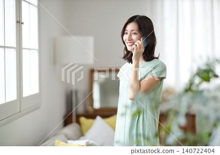 A middle-aged woman talking on her smartphone in the living room. A middle-aged woman talking on her smartphone in the living room. 140722404
