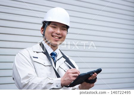 A smiling young man wearing work clothes and a helmet A smiling young man wearing work clothes and a helmet 140722495