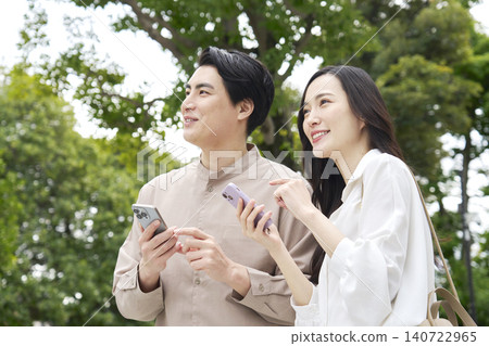 A smiling couple in their 30s talking on their smartphones in a park. A smiling couple in their 30s talking on their smartphones in a park. 140722965