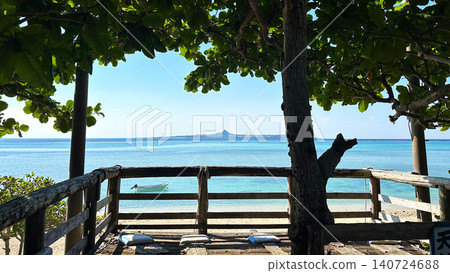 A wooden deck terrace overlooking Okinawa's beautiful emerald green sea and Ie Island floating on the horizon. 140724688