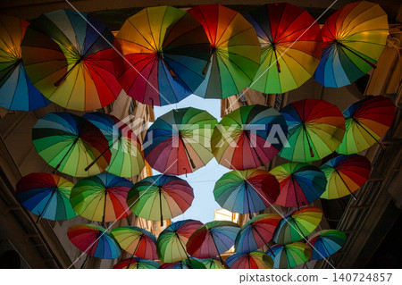 Colorful umbrellas decorate a narrow street in a vibrant neighborhood during a sunny afternoon Colorful umbrellas decorate a narrow street in a vibrant neighborhood during a sunny afternoon 140724857
