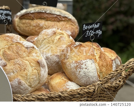Freshly baked artisanal bread loaves in a wicker basket at outdoor market stall display Freshly baked artisanal bread loaves in a wicker basket at outdoor market stall display 140725120