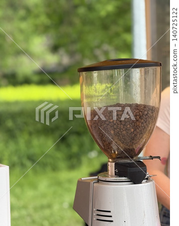 Coffee beans in grinder with blurred green outdoor background, concept of fresh morning brew Coffee beans in grinder with blurred green outdoor background, concept of fresh morning brew 140725122