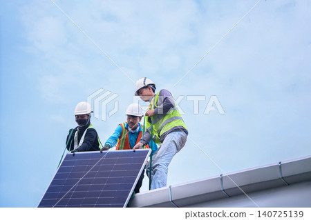 Three Technicians Installing Solar Panel on Rooftop Against Blue Sky Three Technicians Installing Solar Panel on Rooftop Against Blue Sky 140725139
