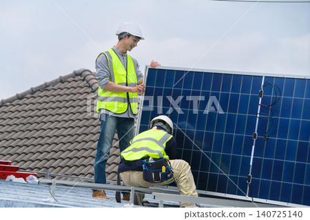 Two Solar Panel Technicians Installing Photovoltaic Panels on Residential Rooftop in Safety Gear Two Solar Panel Technicians Installing Photovoltaic Panels on Residential Rooftop in Safety Gear 140725140