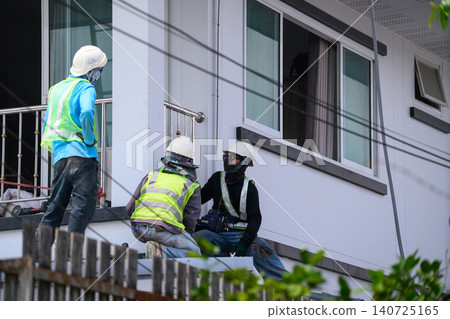 Professional Construction Workers in Safety Gear Inspecting and Repairing Residential Building Exterior Professional Construction Workers in Safety Gear Inspecting and Repairing Residential Building Exterior 140725165