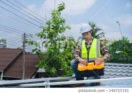 Asian Solar Panel Technician with Toolbox Working on Rooftop Installation Wearing Safety Helmet and High-Vis Vest 140725191