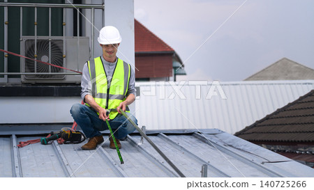 Asian Male Roofer in Safety Vest and Hard Hat Measuring Metal Roof During Construction Work 140725266