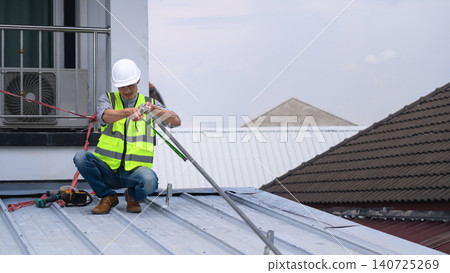 Solar Panel Installer Measuring Metal Roof Rails on Residential Rooftop Wearing Safety Gear Solar Panel Installer Measuring Metal Roof Rails on Residential Rooftop Wearing Safety Gear 140725269
