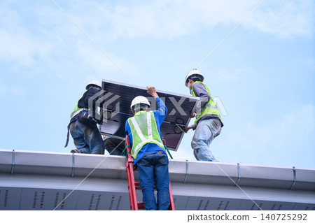 Three Workers Installing Solar Panel on Rooftop with Safety Gear and Ladder Against Blue Sky Three Workers Installing Solar Panel on Rooftop with Safety Gear and Ladder Against Blue Sky 140725292