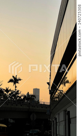 Golden hour cityscape with modern architecture and palm trees silhouetted against the sky 140725308