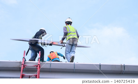 Workers Installing Solar Panel on Rooftop with Safety Gear and Hard Hats Against Blue Sky Workers Installing Solar Panel on Rooftop with Safety Gear and Hard Hats Against Blue Sky 140725419