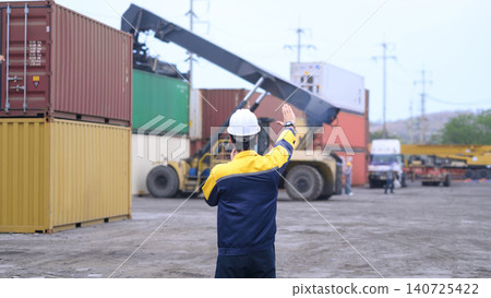 Industrial logistics worker directing container lifting operation at cargo shipping terminal 140725422