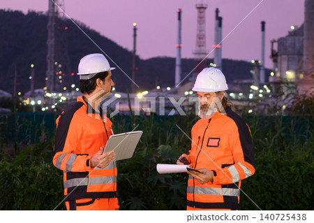 Engineers discussing inspection work outside oil refinery and petrochemical processing facility Engineers discussing inspection work outside oil refinery and petrochemical processing facility 140725438