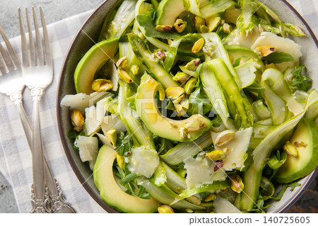 Elegant shaved asparagus parmesan salad with lemon dressing, pistachios, avocado, arugula closeup in the plate. Horizontal top view Elegant shaved asparagus parmesan salad with lemon dressing, pistachios, avocado, arugula closeup in the plate. Horizontal top view 140725605