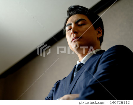 A man in a suit with his arms crossed looks down. A man in a suit with his arms crossed looks down. 140726112