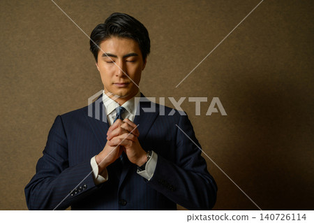 A businessman in a suit prays with his eyes closed. A businessman in a suit prays with his eyes closed. 140726114