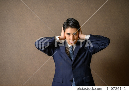 A man in a suit covers his ears, looking confused. A man in a suit covers his ears, looking confused. 140726141