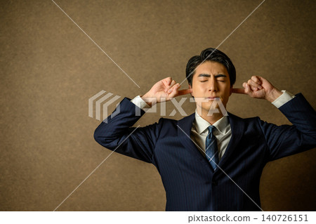 A businessman covers his ears and closes his eyes. A businessman covers his ears and closes his eyes. 140726151