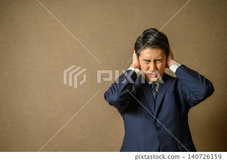 A businessman who covers his ears in anguish A businessman who covers his ears in anguish 140726159