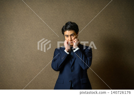 一名身穿西裝的男子雙手捧著雙頰。 一名身穿西裝的男子雙手捧著雙頰。 140726176
