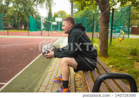 Portrait of basketball player sitting on bench with ball 140726300