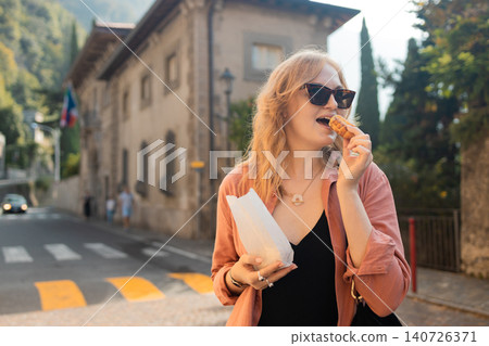 Young blonde woman eating traditional cookie on a city street Young blonde woman eating traditional cookie on a city street 140726371