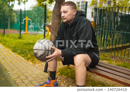 Portrait of basketball player sitting on bench with ball Portrait of basketball player sitting on bench with ball 140726410