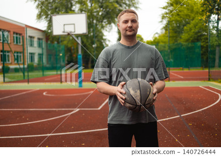 Portrait of young man holding basketball ball on court 140726444