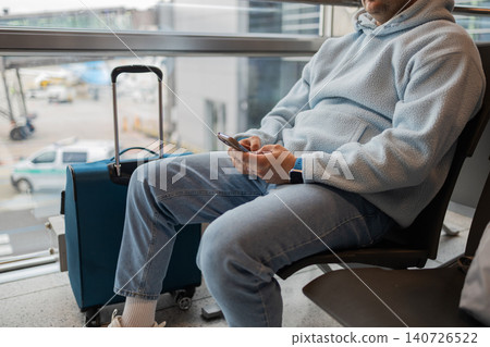 Male traveler waiting at airport terminal with luggage. Passenger waiting for flight departure inside modern airport. Travel, transportation and airport lifestyle concept. Male traveler waiting at airport terminal with luggage. Passenger waiting for flight departure inside modern airport. Travel, transportation and airport lifestyle concept. 140726522