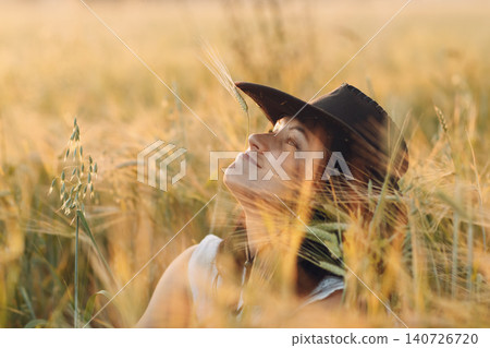 Woman farmer in cowboy hat at agricultural field on sunset. Woman farmer in cowboy hat at agricultural field on sunset. 140726720