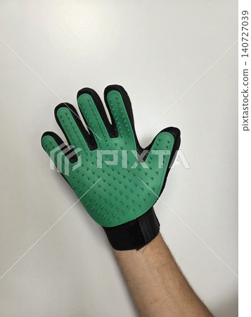 Green pet grooming glove on a human hand isolated on white background. Practical tool for removing loose fur, brushing cats and dogs, and everyday coat care. Green pet grooming glove on a human hand isolated on white background. Practical tool for removing loose fur, brushing cats and dogs, and everyday coat care. 140727039