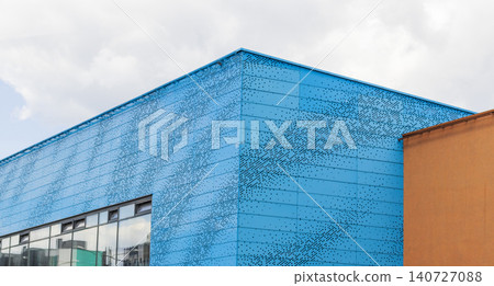 Modern building facade with bright blue perforated metal panels against cloudy sky. Urban Modern building facade with bright blue perforated metal panels against cloudy sky. Urban 140727088